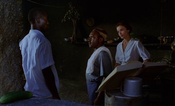 Movie still from “Chocolat” (1988), directed by Claire Denis – A group of people standing next to each other in a room; Medium shot, Over the shoulder angle