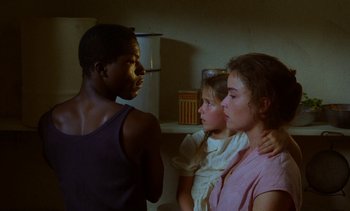 Movie still from “Chocolat” (1988), directed by Claire Denis – A group of people standing next to each other in a room; Close Up shot, Over the shoulder angle