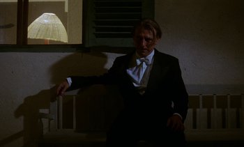 Movie still from “Chocolat” (1988), directed by Claire Denis – A man wearing a suit and tie sitting in front of a window; Medium shot, Low angle