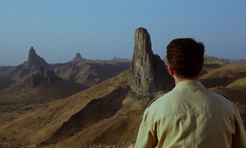 Movie still from “Chocolat” (1988), directed by Claire Denis – A man standing on top of a hill looking at a mountain; Extreme Wide shot, Over the shoulder angle