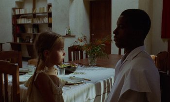 Movie still from “Chocolat” (1988), directed by Claire Denis – A man and a little girl sitting at a dinner table; Medium shot, Over the shoulder angle