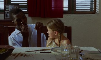 Movie still from “Chocolat” (1988), directed by Claire Denis – A little girl sitting at a table in front of a man; Medium shot, Over the shoulder angle