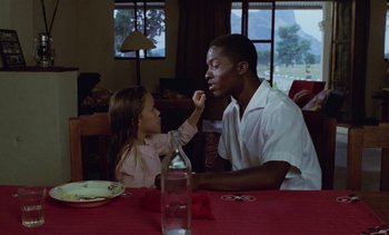Movie still from “Chocolat” (1988), directed by Claire Denis – A little girl feeding a man a piece of food; Medium shot, Over the shoulder angle