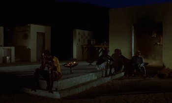 Movie still from “Chocolat” (1988), directed by Claire Denis – A group of people sitting on steps in the dark; Wide shot, High angle
