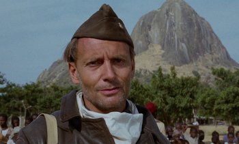 Movie still from “Chocolat” (1988), directed by Claire Denis – A person wearing a hat with a mountain in the background; Close Up shot, Low angle