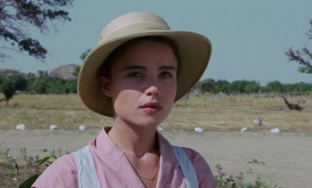 Movie still from “Chocolat” (1988), directed by Claire Denis – A woman wearing a hat standing in a field; Close Up shot, Over the shoulder angle