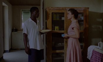 Movie still from “Chocolat” (1988), directed by Claire Denis – A man and a woman standing in front of a wooden cabinet; Medium shot, Over the shoulder angle