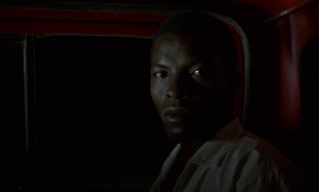 Movie still from “Chocolat” (1988), directed by Claire Denis – A black man with his eyes glowing in the dark; Close Up shot, Over the shoulder angle
