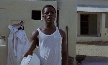 Movie still from “Chocolat” (1988), directed by Claire Denis – A man in a white tank top holding a white frisbee; Medium shot, Low angle