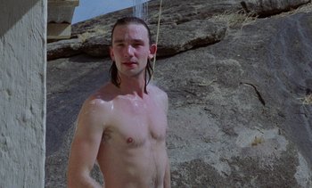 Movie still from “Chocolat” (1988), directed by Claire Denis – A shirtless man standing on top of a cliff; Medium shot, Low angle