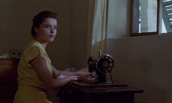 Movie still from “Chocolat” (1988), directed by Claire Denis – A young woman sitting at a sewing machine in front of a window; Medium shot, High angle