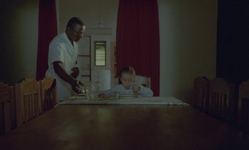 Movie still from “Chocolat” (1988), directed by Claire Denis – A man standing over a girl at a table; Medium shot, Low angle