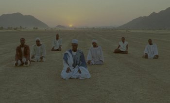 Movie still from “Chocolat” (1988), directed by Claire Denis – A group of men sitting on the ground in the desert; Extreme Wide shot, High angle