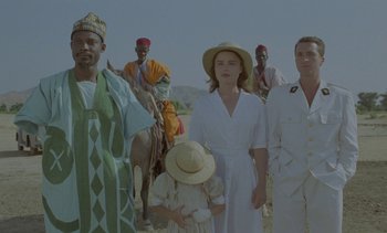Movie still from “Chocolat” (1988), directed by Claire Denis – A group of people standing next to each other on a dirt road; Medium shot, Low angle