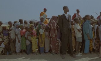 Movie still from “Chocolat” (1988), directed by Claire Denis – A group of people standing in front of each other on a dirt ground; Wide shot, Low angle