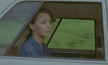Movie still from “Chocolat” (1988), directed by Claire Denis – A woman sitting in the driver's seat of a car; Close Up shot, Over the shoulder angle