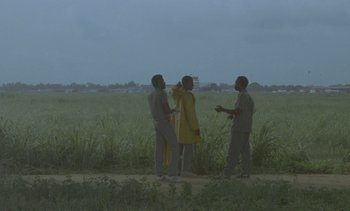Movie still from “Chocolat” (1988), directed by Claire Denis – Three men standing on a dirt road near a field; Extreme Wide shot, Low angle