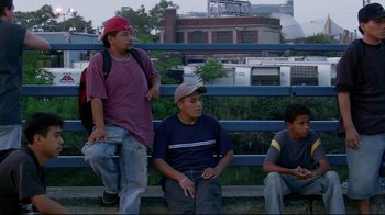 Movie still from “Chop Shop” (2007), directed by Ramin Bahrani – A group of men sitting on a bench next to each other; Medium shot, Low angle