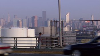 Movie still from “Chop Shop” (2007), directed by Ramin Bahrani – A man standing on the side of a road near a fence; Extreme Wide shot, Low angle