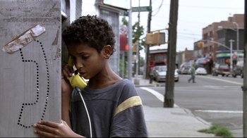 Movie still from “Chop Shop” (2007), directed by Ramin Bahrani – A young boy holding a banana while talking on a phone; Close Up shot, High angle
