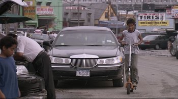 Movie still from “Chop Shop” (2007), directed by Ramin Bahrani – A man riding a scooter next to a car on the street; Wide shot, Low angle