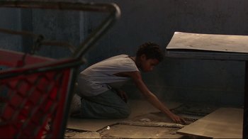 Movie still from “Chop Shop” (2007), directed by Ramin Bahrani – A young man kneeling on the ground using a laptop; Medium shot, Overhead angle