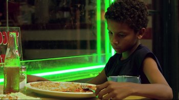 Movie still from “Chop Shop” (2007), directed by Ramin Bahrani – A young boy sitting at a table with a plate of pizza; Close Up shot, Low angle