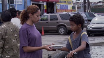 Movie still from “Chop Shop” (2007), directed by Ramin Bahrani – A woman handing a box to a young boy on the side of the road; Medium shot, Over the shoulder angle