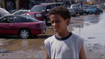 Movie still from “Chop Shop” (2007), directed by Ramin Bahrani – A young boy standing on a wet street near parked cars; Close Up shot, High angle