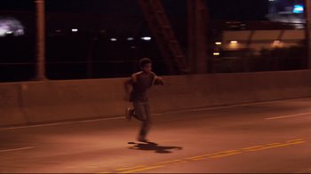 Movie still from “Chop Shop” (2007), directed by Ramin Bahrani – A man riding a skateboard down the side of a road; Wide shot, High angle