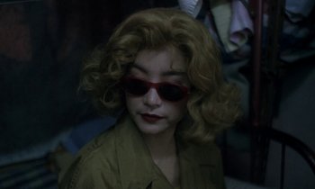 Movie still from “Chungking Express” (1994), directed by Kar-Wai Wong – A woman wearing a red sunglasses and a brown jacket; Close Up shot, Over the shoulder angle