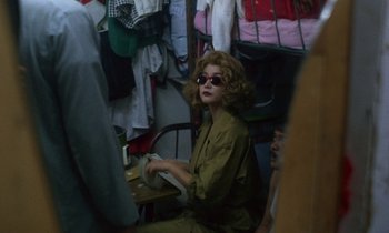 Movie still from “Chungking Express” (1994), directed by Kar-Wai Wong – A woman sitting on a chair in front of a bunch of clothes; Medium shot, Over the shoulder angle