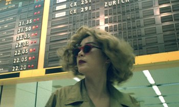 Movie still from “Chungking Express” (1994), directed by Kar-Wai Wong – A woman in sunglasses standing in front of an airport sign; Medium shot, Low angle