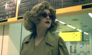 Movie still from “Chungking Express” (1994), directed by Kar-Wai Wong – A woman with blonde curly hair wearing sunglasses and a tan jacket; Close Up shot, Low angle