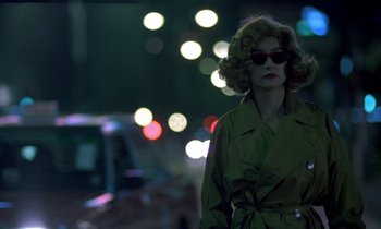 Movie still from “Chungking Express” (1994), directed by Kar-Wai Wong – A woman in a green trench coat standing on a street; Medium shot, Over the shoulder angle