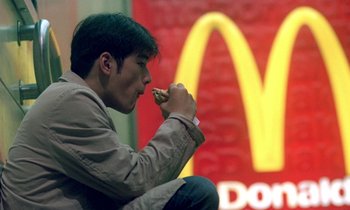 Movie still from “Chungking Express” (1994), directed by Kar-Wai Wong – A man sitting in front of a mcdonald's sign eating a piece of food; Medium shot, High angle