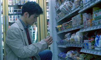 Movie still from “Chungking Express” (1994), directed by Kar-Wai Wong – A man sitting on the ground looking at his cell phone; Medium shot, Over the shoulder angle