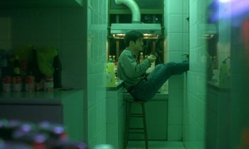 Movie still from “Chungking Express” (1994), directed by Kar-Wai Wong – A man sitting on top of a stool in a kitchen; Wide shot, High angle