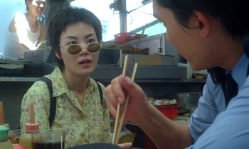 Movie still from “Chungking Express” (1994), directed by Kar-Wai Wong – A woman wearing sunglasses and holding chopsticks in her hand; Close Up shot, Over the shoulder angle