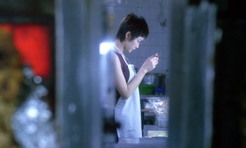 Movie still from “Chungking Express” (1994), directed by Kar-Wai Wong – A woman standing in a kitchen looking at her cell phone; Medium shot, Low angle