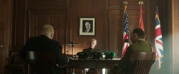 Movie still from “Churchill” (2017), directed by Jonathan Teplitzky – A man sitting at a desk in front of an american flag; Medium shot, Low angle