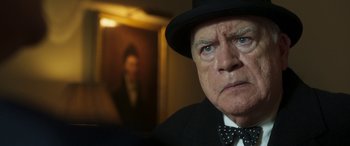 Movie still from “Churchill” (2017), directed by Jonathan Teplitzky – An older man wearing a hat and a bow tie; Close Up shot, Over the shoulder angle