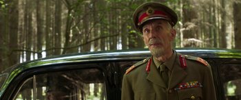 Movie still from “Churchill” (2017), directed by Jonathan Teplitzky – An older man in a military uniform standing next to a car; Medium shot, Over the shoulder angle