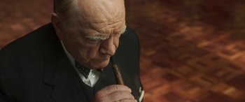 Movie still from “Churchill” (2017), directed by Jonathan Teplitzky – An older man in a suit and bow tie holding a cigar; Close Up shot, Over the shoulder angle