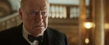 Movie still from “Churchill” (2017), directed by Jonathan Teplitzky – An older man in a suit and bow tie; Close Up shot, Over the shoulder angle