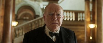 Movie still from “Churchill” (2017), directed by Jonathan Teplitzky – An older man wearing a suit and a bow tie; Close Up shot, Low angle
