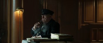 Movie still from “Churchill” (2017), directed by Jonathan Teplitzky – An old man sitting at a desk smoking a cigarette; Medium shot, Low angle