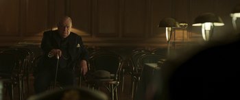 Movie still from “Churchill” (2017), directed by Jonathan Teplitzky – A man sitting in front of a bunch of chairs; Medium shot, Over the shoulder angle