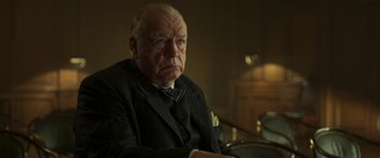 Movie still from “Churchill” (2017), directed by Jonathan Teplitzky – An older man in a suit and tie sitting in a chair; Close Up shot, Low angle