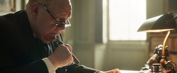 Movie still from “Churchill” (2017), directed by Jonathan Teplitzky – An older man with glasses is holding a pen; Close Up shot, Over the shoulder angle